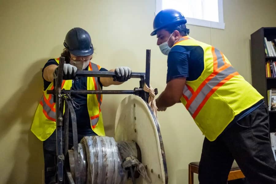 Deux techniciens installant la gaine depuis l'intérieur du bâtiment, sans excavation
