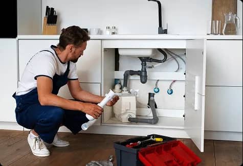 Plombier accroupi remplaçant un siphon sous un comptoir de cuisine