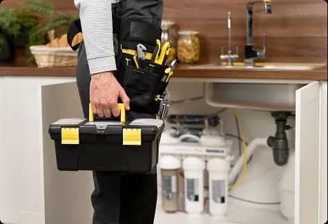 Plombier transportant sa boîte à outils dans une cuisine