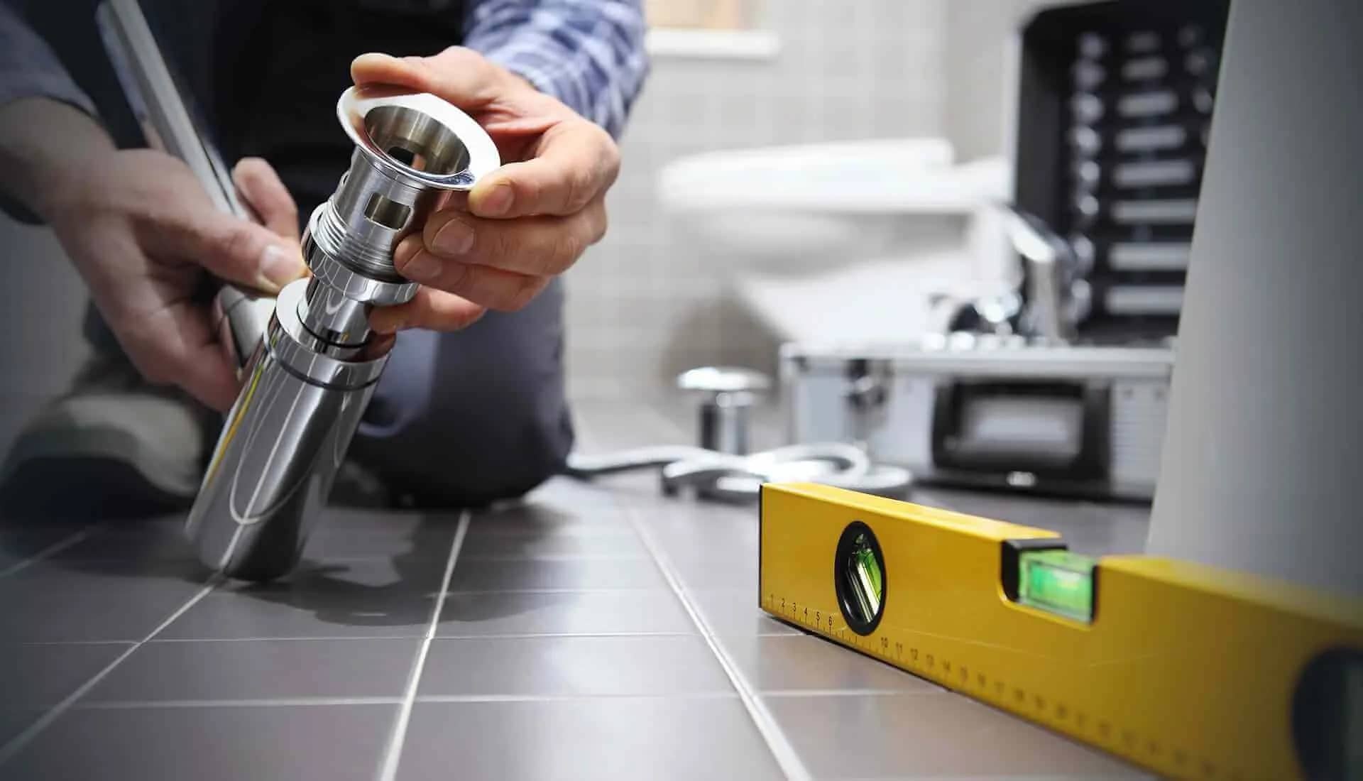 Plombier assemblant un siphon chromé au sol d'une salle de bain