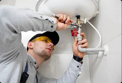 Plumber in yellow safety glasses repairing a water heater valve